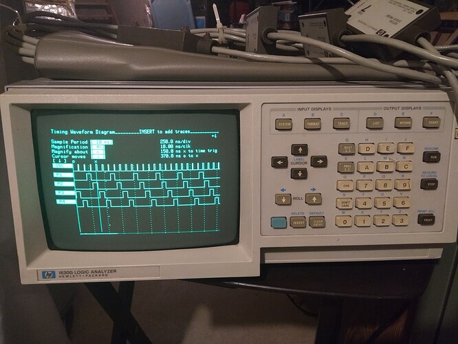 A HP 1630G logic analyzer showing five traces in timing mode.  It has a green phosphor CRT on the left and a variety of keypad buttons on the right.The traces show a short duty cycle oscillator on at the top, with four divide-by-four phase traces below it.