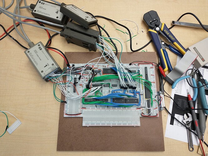The same breadboard is now surrounded by a variety of tools, including several pairs of pliers, a wire stripper, and a small adjustable wrench on the right.  The same logic analyzer pods from previous photos are above the boards, with a slew of flying leads coming in to the ICs that were labeled as buffers in the previous image.